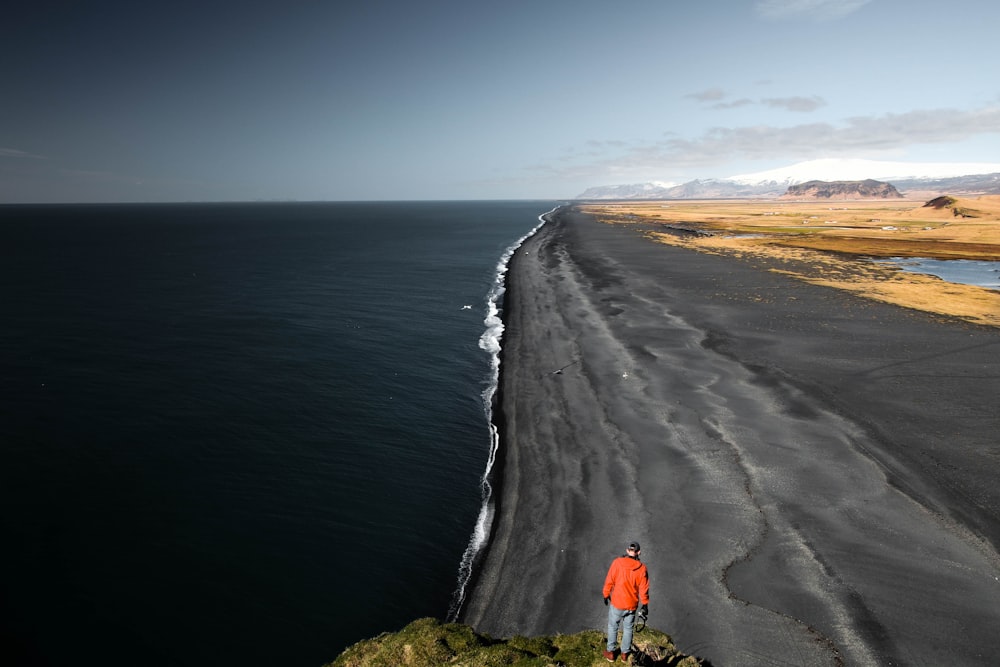 Hombre en la parte superior roja de pie cerca del acantilado con vistas a la orilla del mar durante el día