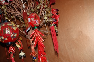 A decorative display featuring red and gold objects hung on branches. The items include red tassels, lanterns with Chinese characters, and some gold ornaments. The arrangement creates a festive and cultural atmosphere.