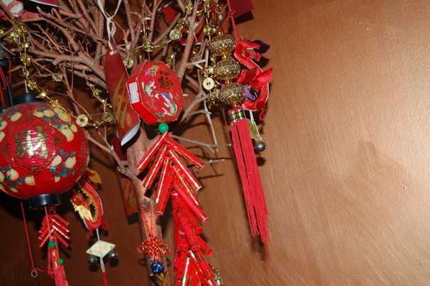 A decorative display featuring red and gold objects hung on branches. The items include red tassels, lanterns with Chinese characters, and some gold ornaments. The arrangement creates a festive and cultural atmosphere.