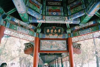 Intricate and colorful traditional architecture with ornate designs and calligraphy. The structure features a richly painted wooden ceiling with decorative panels and vibrant motifs.