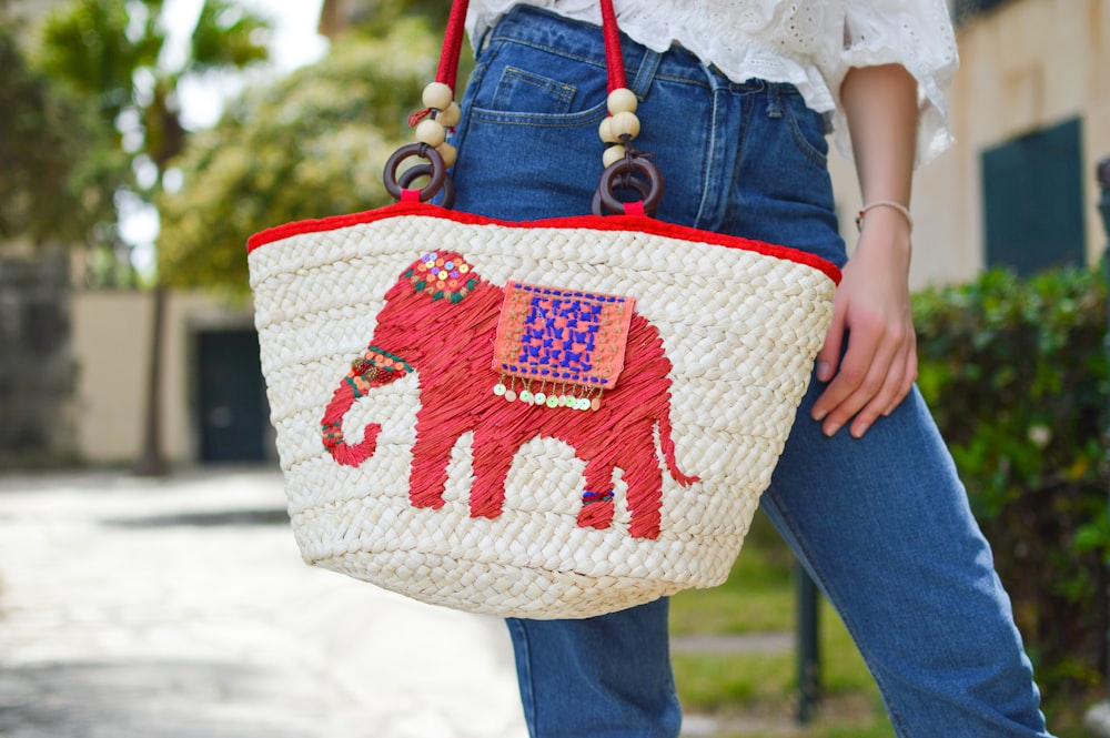 Persona sosteniendo la bolsa de mano gráfica del elefante blanco y rojo Foto de primer plano