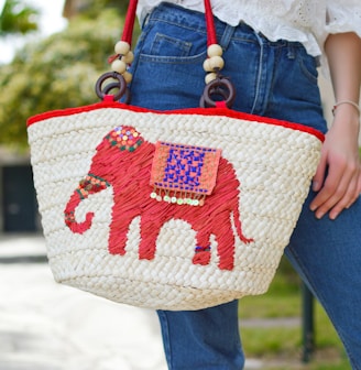 person holding white and red elephant graphic tote bag close-up photo