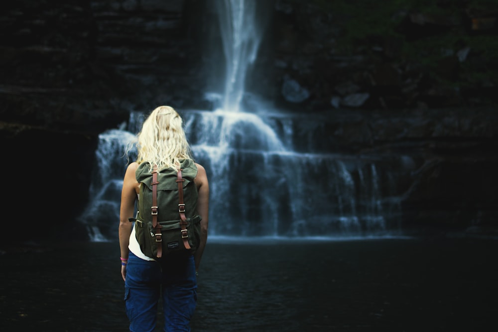 fotografía de enfoque superficial de mujer con mochila frente a cascadas de agua