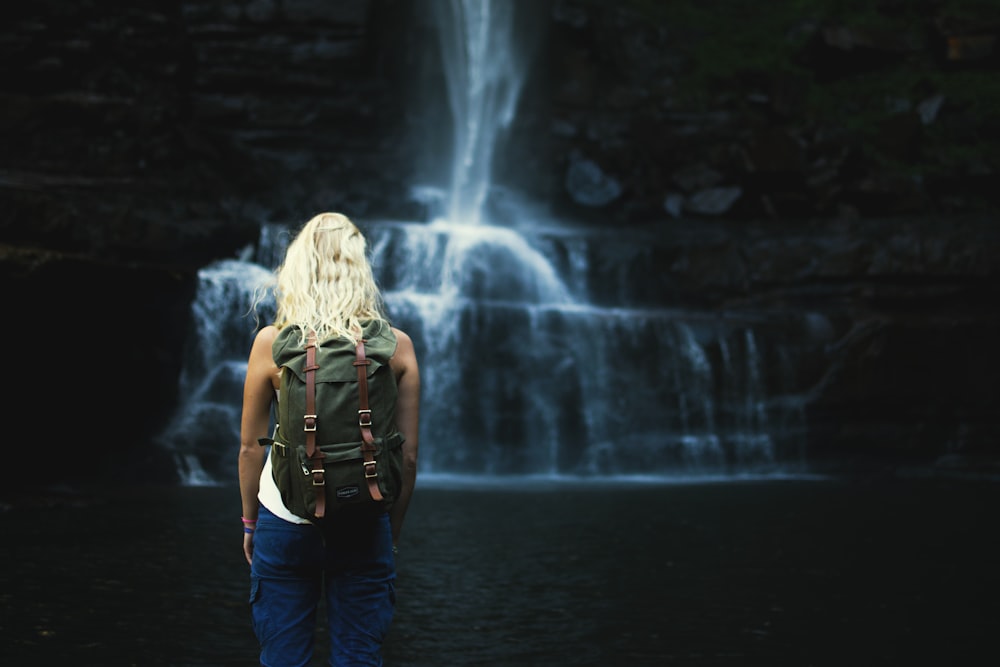 shallow focus photography of woman with backpack in front of water falls