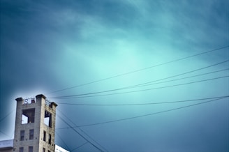 A tall, narrow building with a large S logo and an open top area is situated to the left. Overhead wires stretch across the sky, which is a vibrant gradient of blue. The building seems isolated against the expansive sky.