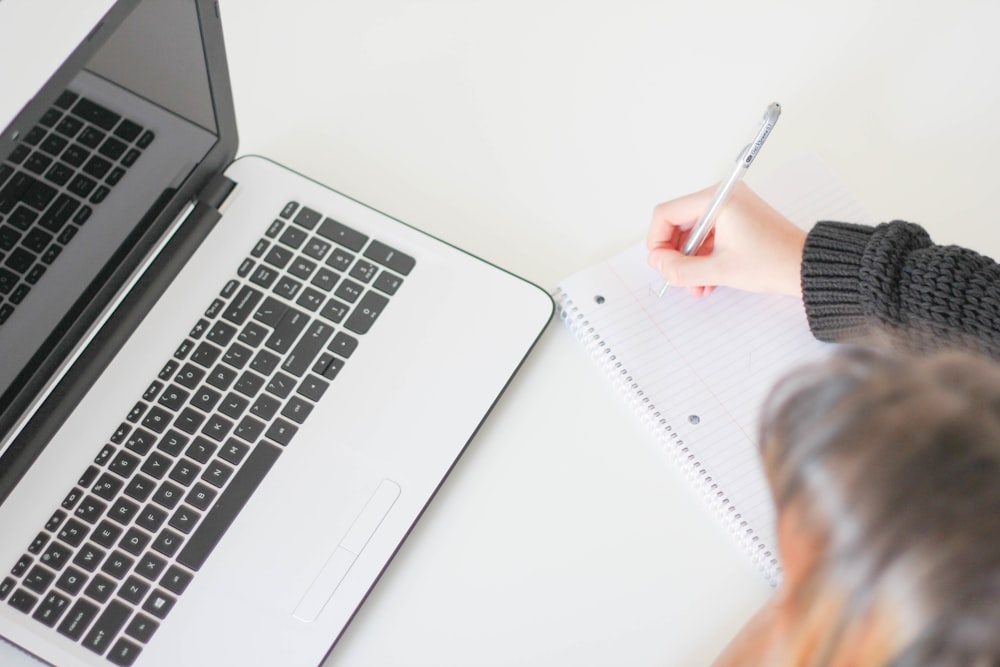 A woman taking notes in a large notebook next to a laptop