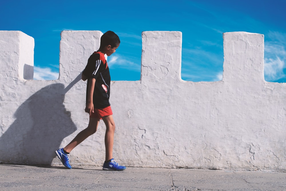 boy walking beside white concrete wall