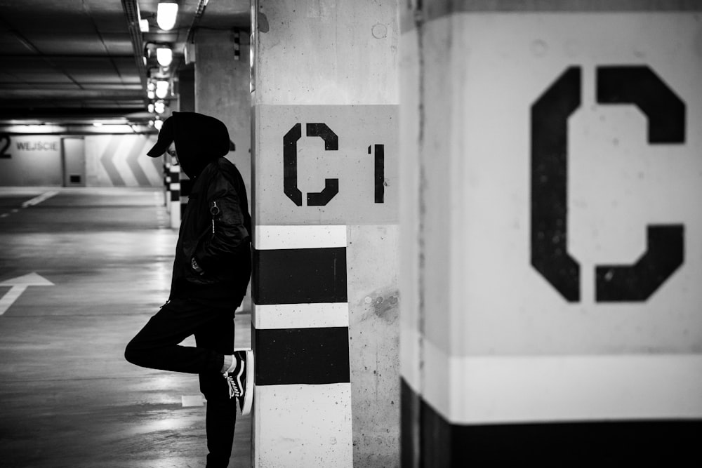 grayscale photo of man leaning on post