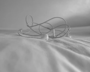 A pair of colorful earbuds tangled playfully on a vibrant fabric surface.