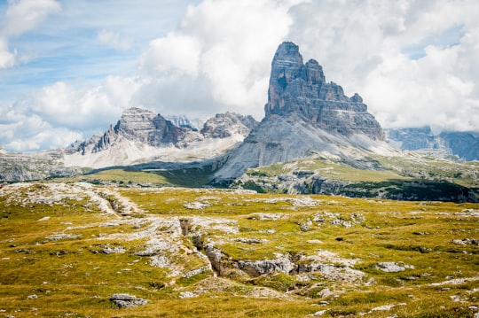 rock formation on wide field grass under cloudy blue sky during daytime in Dolomites Italy