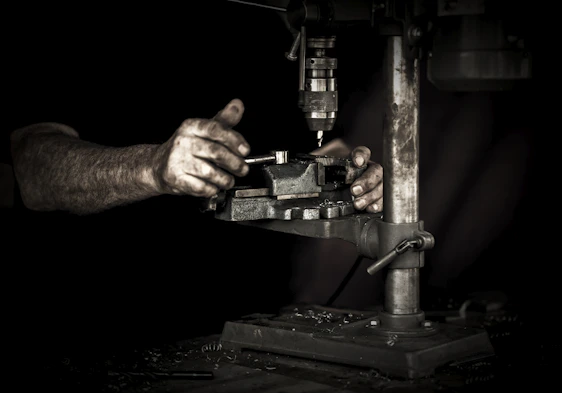 Close-up of rugged hands gripping a power drill in a gritty workshop setting, surrounded by metal tools and wood.
