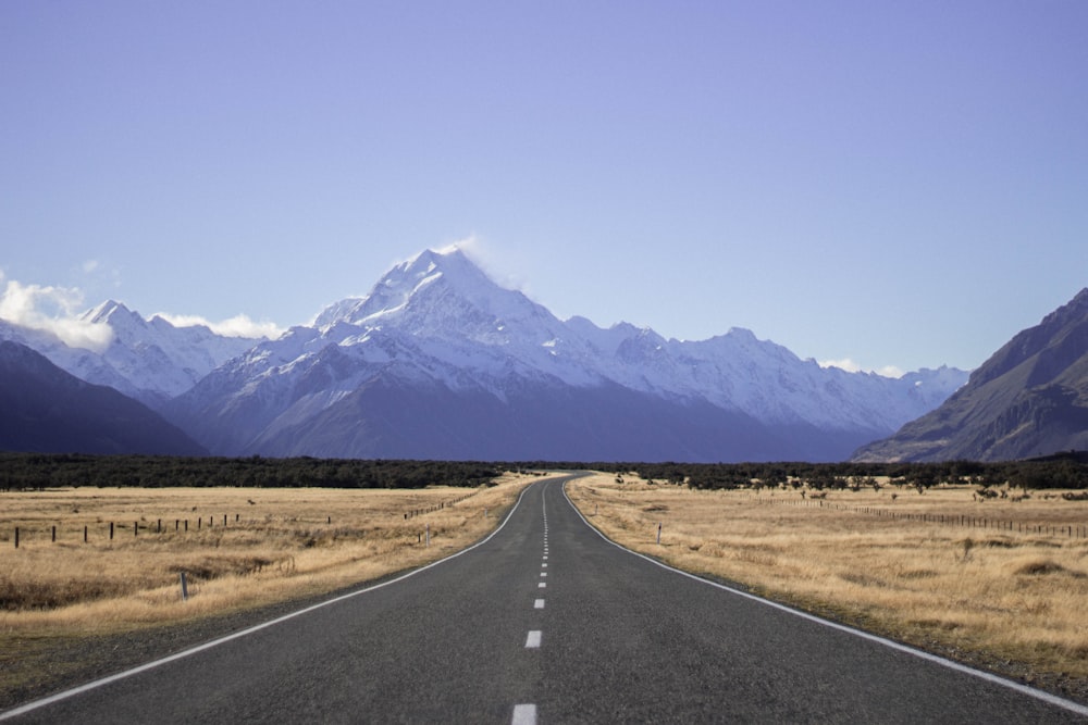 landscape photography of empty dessert road under blue calm sky with mountain view