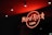 A neon sign displaying the words 'Hard Rock Cafe' in bright red is illuminated against a dark background. The ceiling is adorned with recessed lighting.