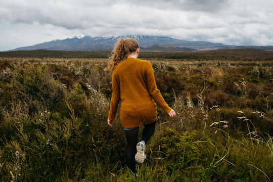 woman walking in grass field under stratocomulus clouds in Tongariro National Park New Zealand