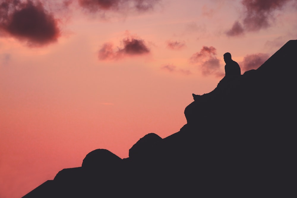 silhouette of man sitting on cliff