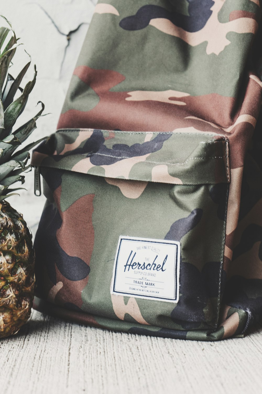 Ausgeschnittene Aufnahme eines Camouflage-Rucksacks und eines Teils einer Ananas.