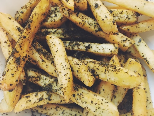 A close-up view of crispy French fries seasoned with herbs and spices, piled together.