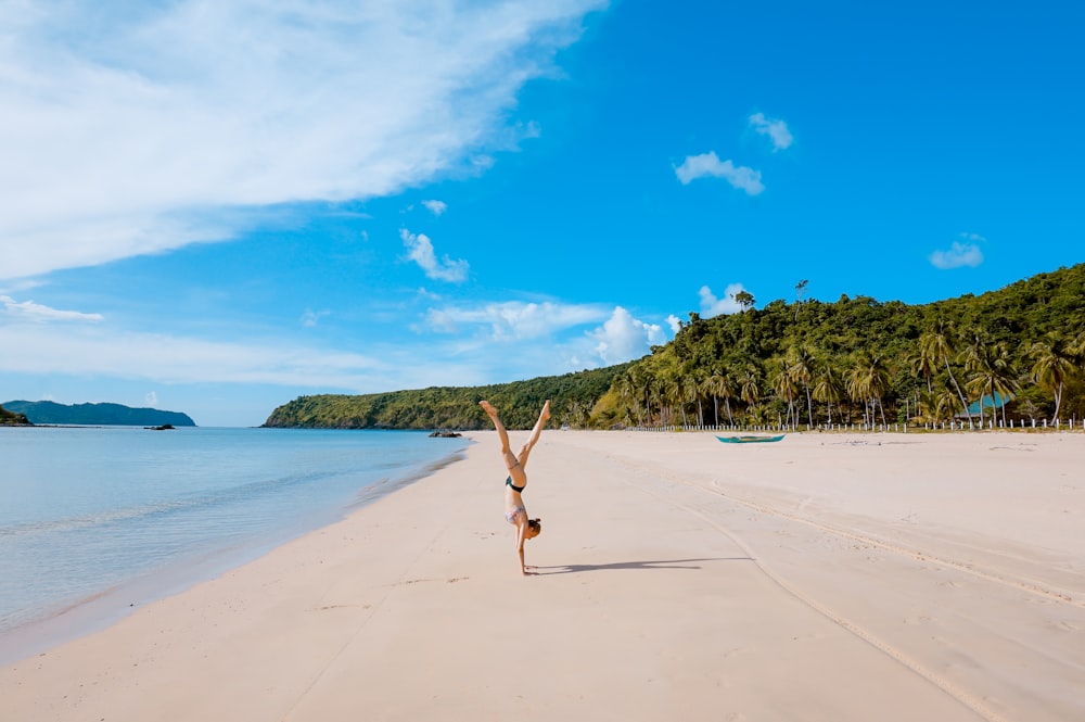 woman doing acrobatic on seashore near mountain range under cumulus clouds