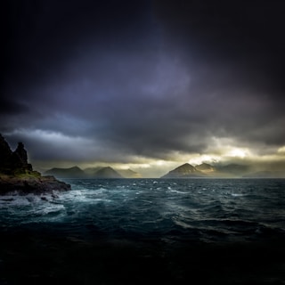 landscape photo of waters, mountains, and black clouds