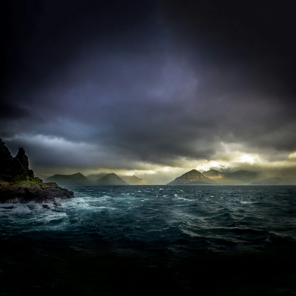 landscape photo of waters, mountains, and black clouds