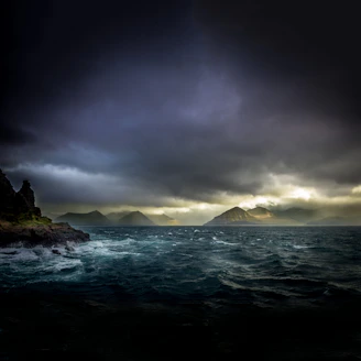 landscape photo of waters, mountains, and black clouds