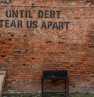 Until debt tear us apart printed red brick wall at daytime