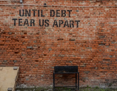 Until debt tear us apart printed red brick wall at daytime