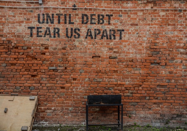 Until debt tear us apart printed red brick wall at daytime