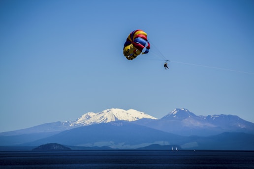 A colorful parachute with a person gliding over a scenic coastline.