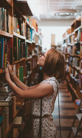 woman standing between library book shelves