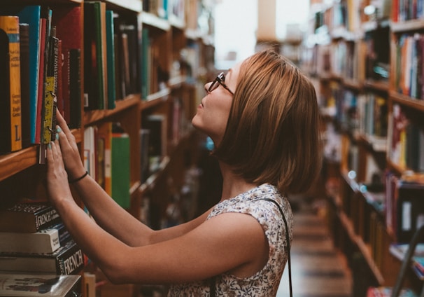 woman standing between library book shelves