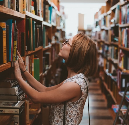 woman standing between library book shelves