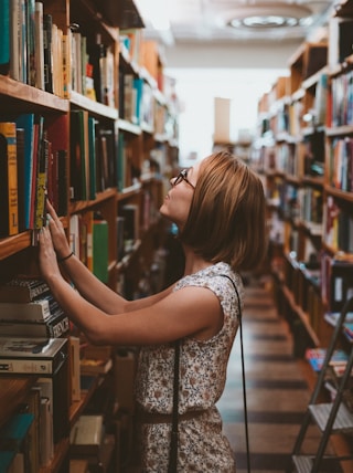 woman standing between library book shelves