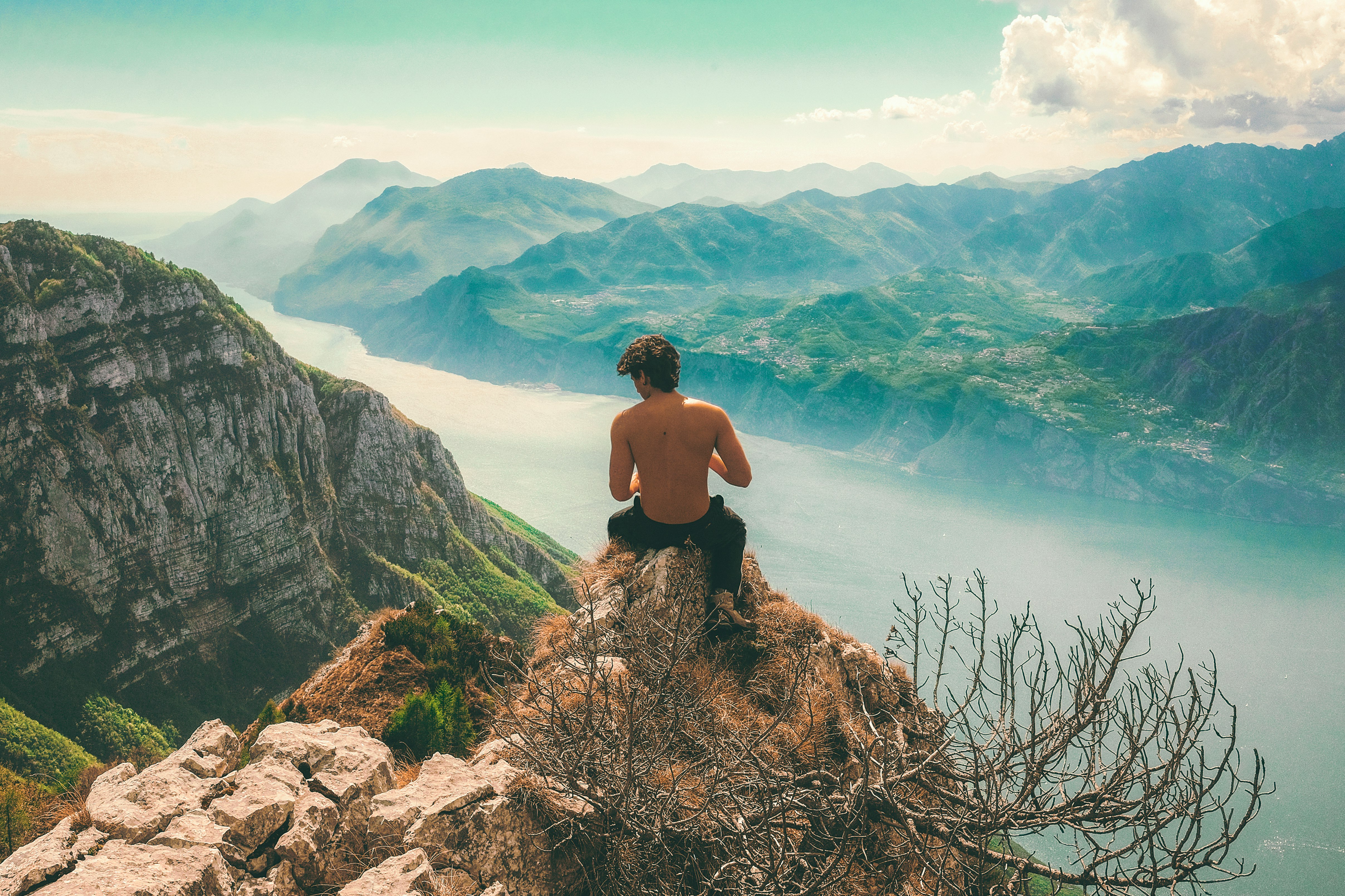 man seating on top of cliff in front of mountains