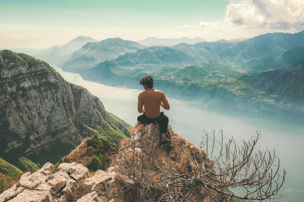 homem sentado no topo do penhasco na frente das montanhas