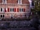 A charming, historic brick building with red shutters and a red-tiled roof sits in a European street setting. Bicycles are parked along the canal in front, and small potted plants line the stone edge. An Italian flag hangs on the left side of the building, indicating the presence of an Italian restaurant.