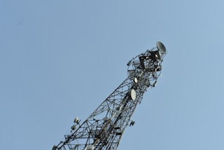 A tall communication tower with multiple satellite dishes and antennas on a clear day. The structure is an intricate lattice of metal.