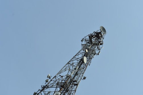 A tall communication tower with multiple satellite dishes and antennas on a clear day. The structure is an intricate lattice of metal.