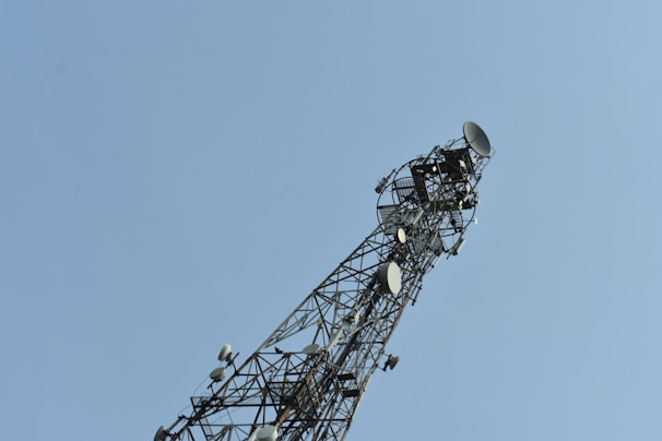 A tall communication tower with multiple satellite dishes and antennas on a clear day. The structure is an intricate lattice of metal.