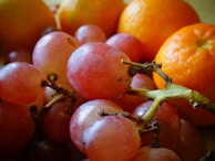 A close-up of ripe oranges and grapes on a wooden table.