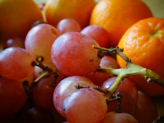 A close-up of ripe oranges and grapes on a wooden table.