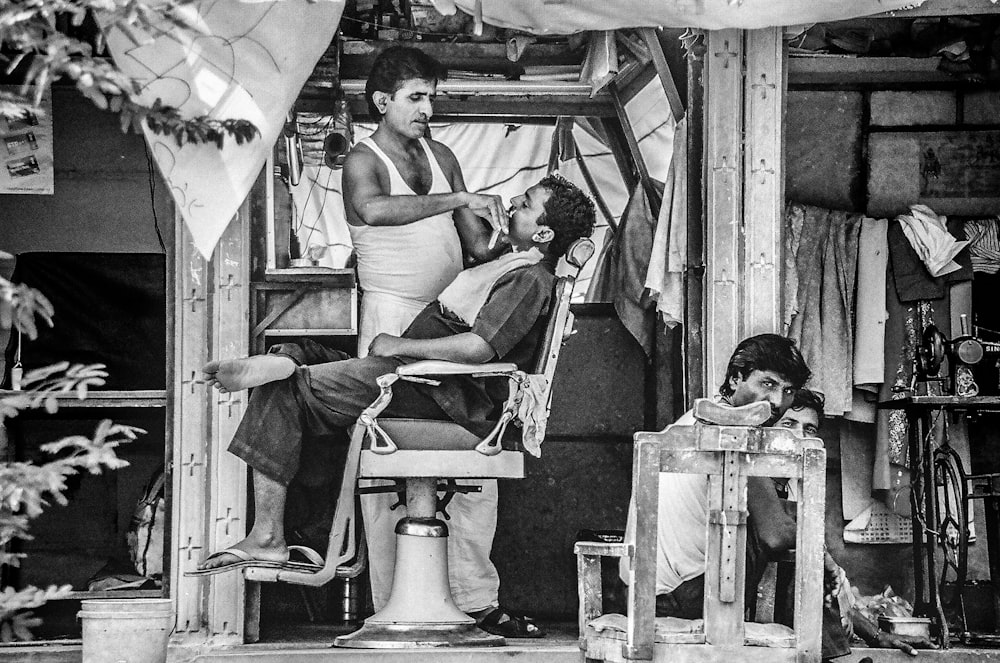 grayscale photo of barber trimming man's beard