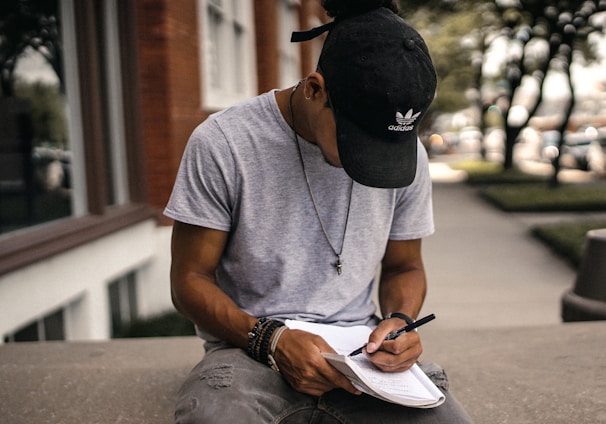 person in black adidas cap sitting on bench writing on notebook