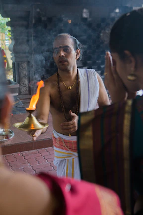 A young boy dressed in a cream-colored kurta pajama, holding a small brass diya.