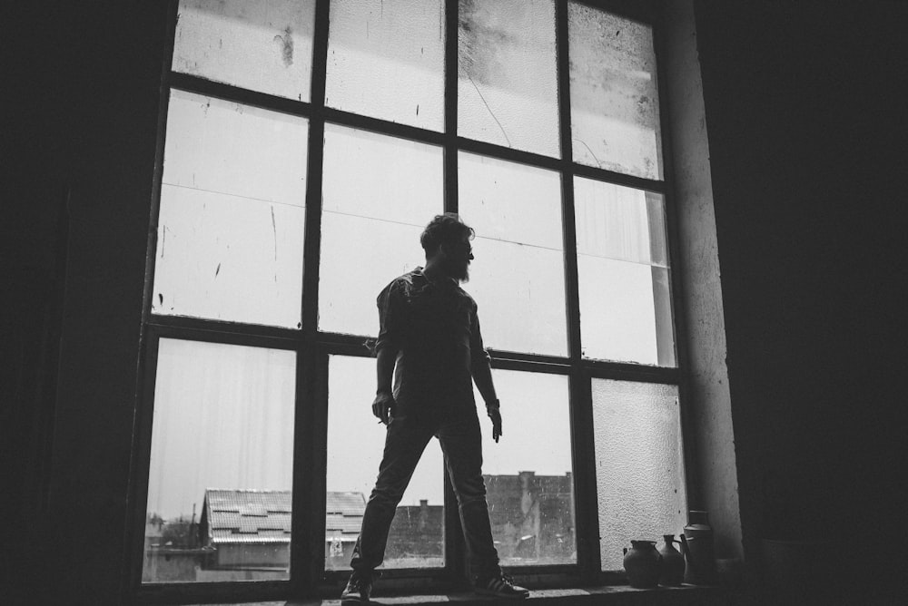 man standing against the glass window grayscale photography