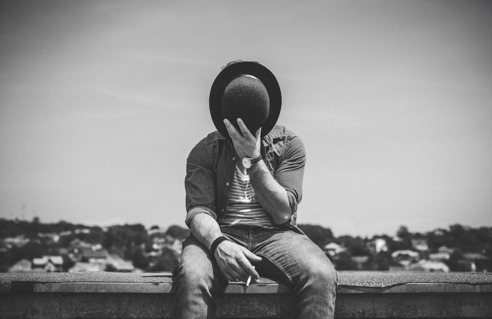 a man sitting on a ledge with a hat covering his face