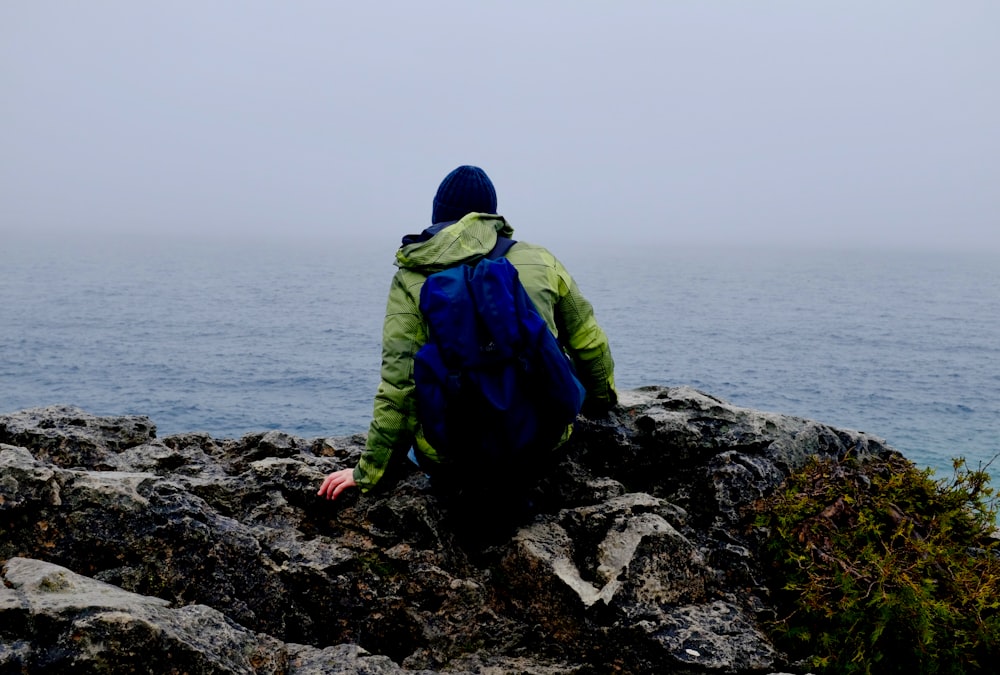 person sitting on rock near body of water during day time