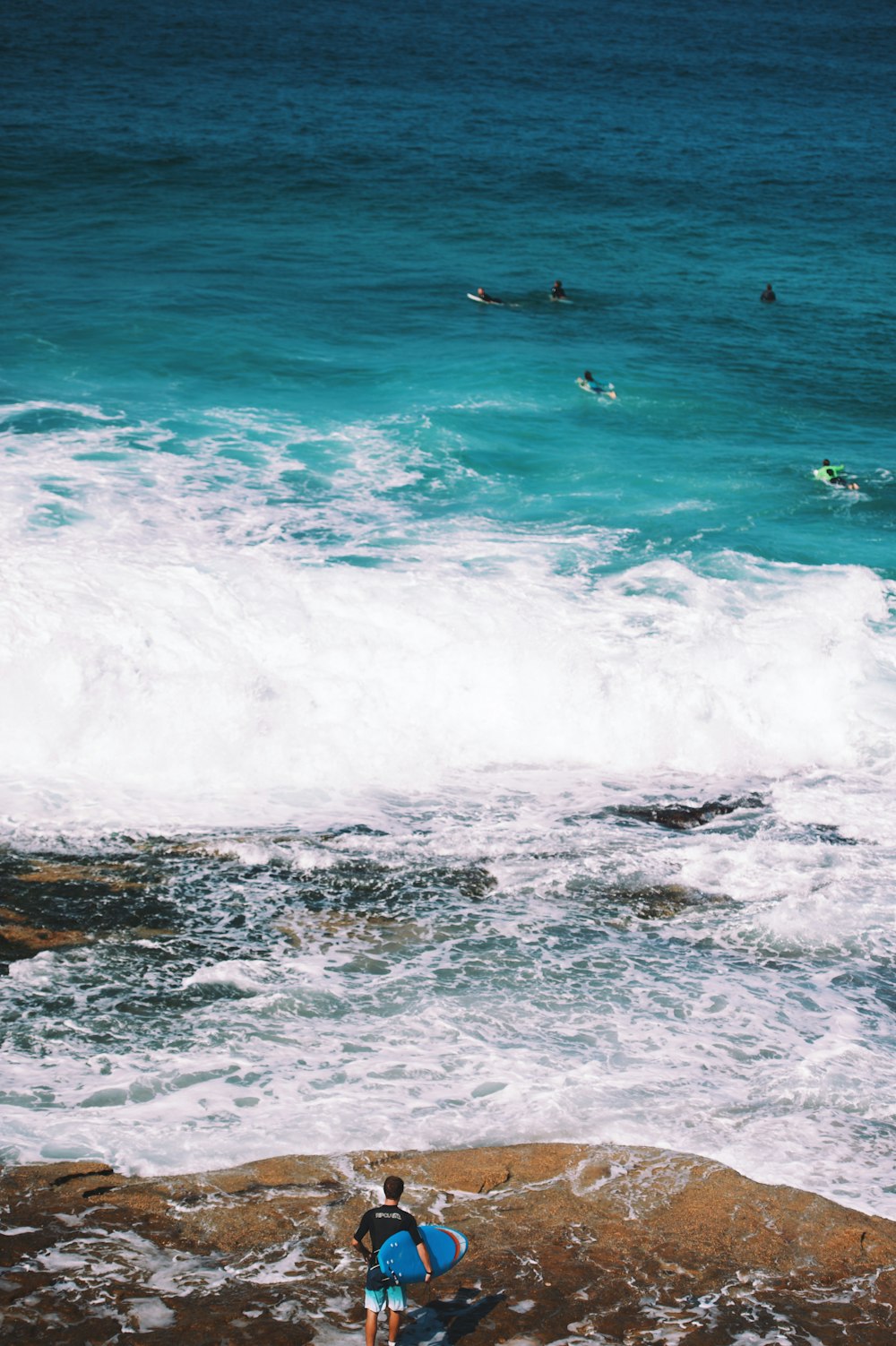 Mann mit blauem Surfbrett, der am Meeresufer steht