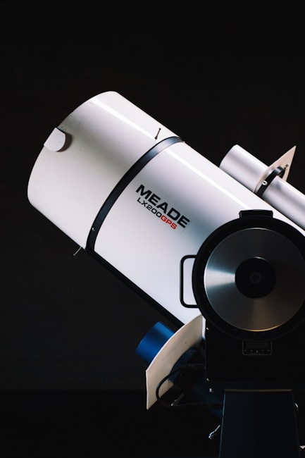 A close-up view of a Meade LX200GPS telescope against a dark background. The telescope appears sleek and futuristic, with a cylindrical body and a large lens at the front.