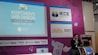 A speaker is presenting at a technology-themed event, with a backdrop displaying a title about responsive web design. The backdrop is colorful with purple and blue tones, featuring multiple logos, including IECE, CIESPAL, and Campus Party. The speaker stands at a podium with a microphone, and there is a partial view of the audience area.